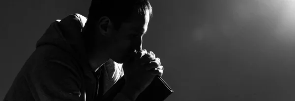Religijny młody człowiek modli się do Boga na ciemnym tle, czarny i — Zdjęcie stockowe
