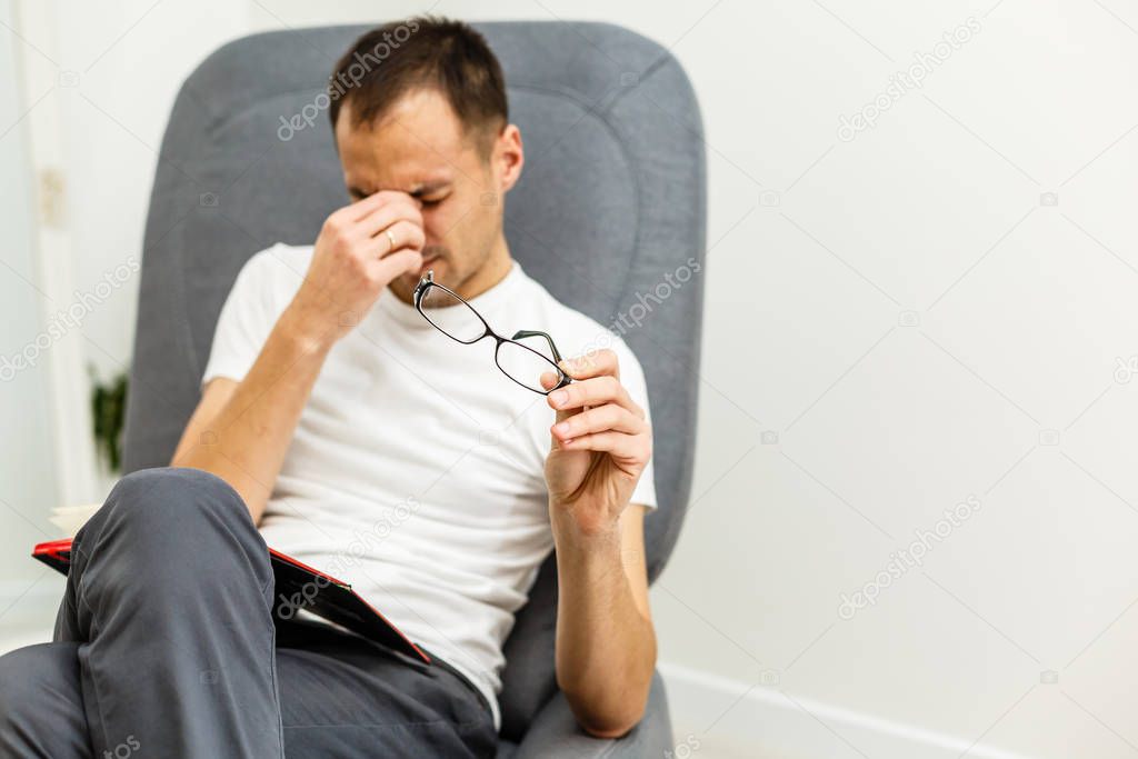 Man with tired eyes after long work holding his eyeglasses