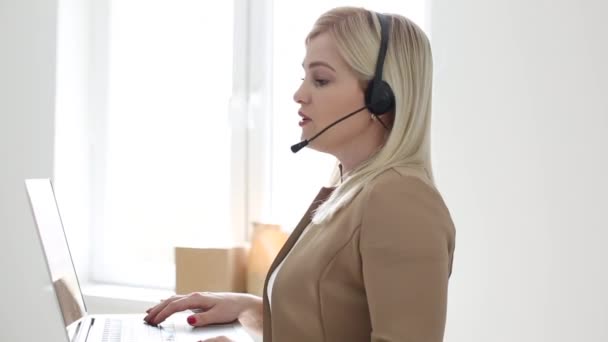 Kendine güvenen kadın ofis çalışanı kulaklık takıyor ve dizüstü bilgisayara bakıyor. Genç iş kadını müşteri hizmetleri müdürü uzaktan iletişim kuran webcam ile konuşuyor.. — Stok video