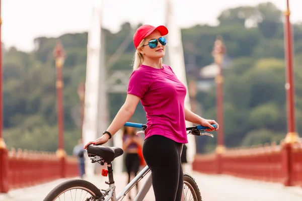 Jovem mulher de bicicleta de pé na estrada e olhando para algum lugar — Fotografia de Stock