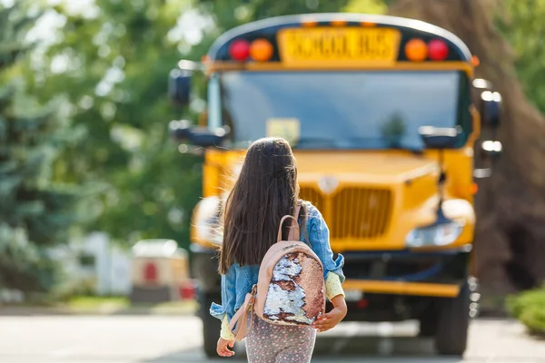 Niña parada junto a una gran puerta de autobús escolar con su mochila rosa . — Foto de Stock