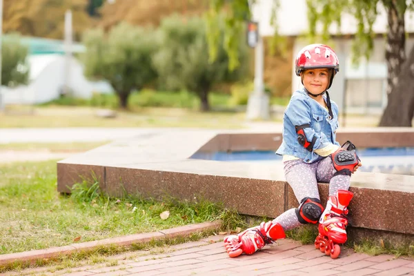 롤러스케이트를 타고 공원 벤치에 앉아 있는 세 어린이 — 스톡 사진