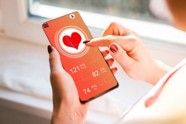 Kadın kanepede oturuyor ve elinde sağlık kartı takibi uygulaması olan bir telefon tutuyor.