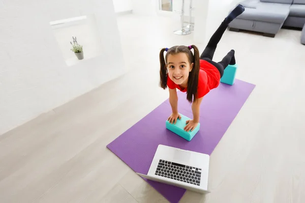 Quarantine at home. little girl doing yoga olnline on a laptop during self isolation quarantine — Stock Photo, Image