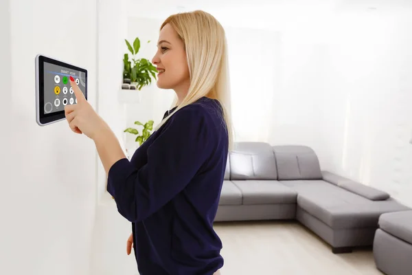 Smart House. Nette, fröhliche Frau schaut auf die Sensorscheibe, während sie sie drückt — Stockfoto