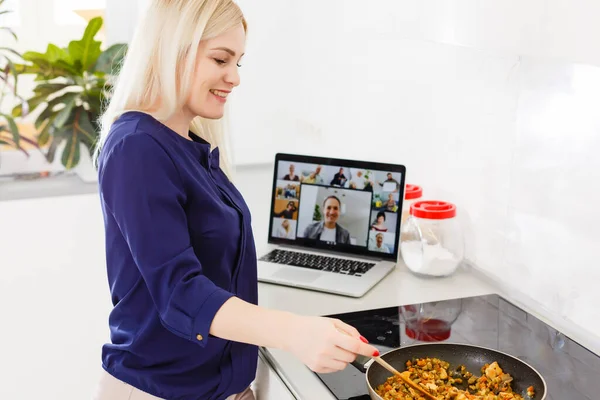 Jonge vrouw kookt in de voorkant open laptop en videochating in de keuken — Stockfoto