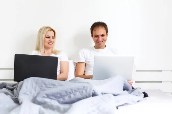 Pareja en el portátil en la cama trabajando en computadoras separadas. Joven pareja interracial moderna, mujer, hombre caucásico, ver con espacio de copia . — Foto de Stock