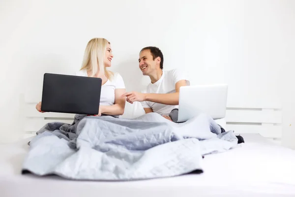 Een paar op een laptop in bed werken op aparte computers. jong modern interraciaal koppel, vrouw, blanke man, uitzicht met kopieerruimte. — Stockfoto