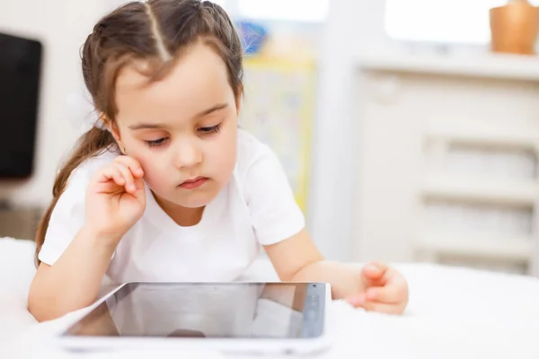 Curiosa bambina che si diverte usando il tablet digitale da sola seduta sul pavimento, felice bambino in età prescolare intelligente che gioca con il computer guardando lo schermo guardare cartoni animati online a casa — Foto Stock