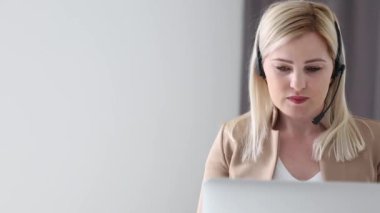 Kendine güvenen kadın ofis çalışanı kulaklık takıyor ve dizüstü bilgisayara bakıyor. Genç iş kadını müşteri hizmetleri müdürü uzaktan iletişim kuran webcam ile konuşuyor..