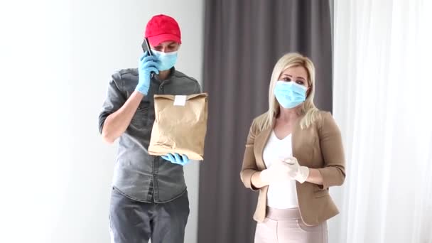 Un corriere con maschera e guanti protettivi consegna un pacco. Lavorare in una pandemia — Video Stock