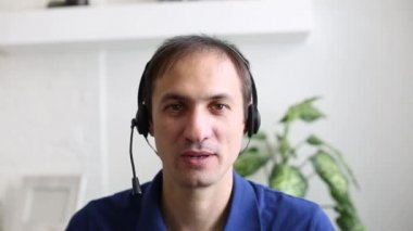 Mavi gömlekli ve kameraya gülümseyen bir adam.