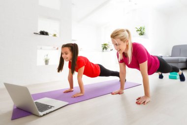 Anne ve kızı koronavirüs salgını sırasında evde karantina izolasyonu dersinde yoga dersi veriyorlar. Aile evden birlikte spor yapıyor. Sağlıklı yaşam tarzı