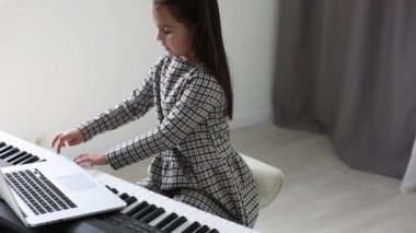 Küçük kız çevrimiçi müzik dersi izliyor ve evden ders çalışıyor. Küçük bir kız bilgisayar ekranına bakarken piyano becerilerini geliştiriyor..