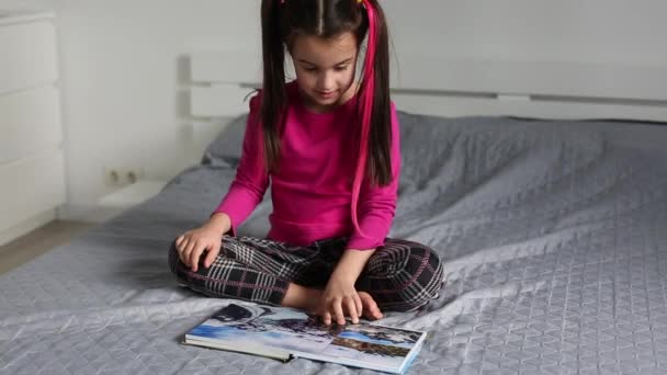 Niña viendo un libro de fotos en casa. La mano se mueve a través de la página. — Vídeos de Stock