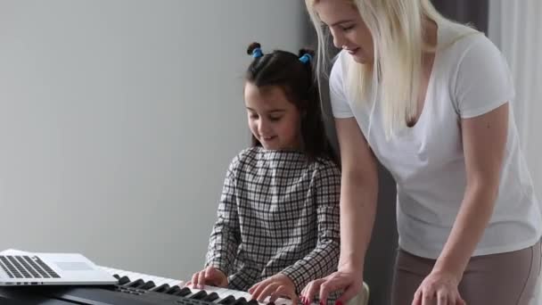 Niña viendo la lección de música en línea y estudiando desde casa. jovencita practicando sus habilidades de piano mientras mira la pantalla de ordenador siguiendo a la profesora en una videollamada.. — Vídeo de stock