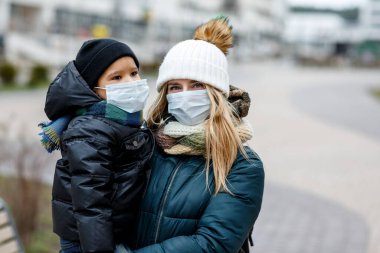 Şehirdeki sokakta maskeli çocukların olduğu bir aile. Anne ve çocuk koronavirüs ve grip salgını sırasında yüz maskesi takıyor. Virüs ve hastalık koruması, kalabalık yerlerde el dezenfektanı..