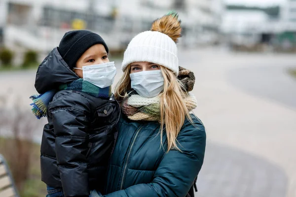 Family with kids in face mask on the street in the city. Mother and child wear facemask during coronavirus and flu outbreak. Virus and illness protection, hand sanitizer in public crowded place.
