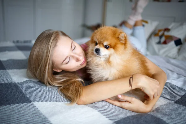 Mutlu sarışın kadın köpeği Spitz ile yatakta uzanıyor. Bir kadın ve bir köpeğin portresi..