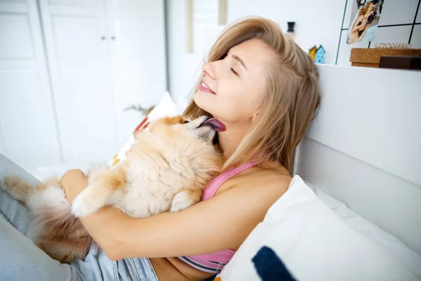Mutlu sarışın kadın köpeği Spitz ile yatakta uzanıyor. Bir kadın ve bir köpeğin portresi..