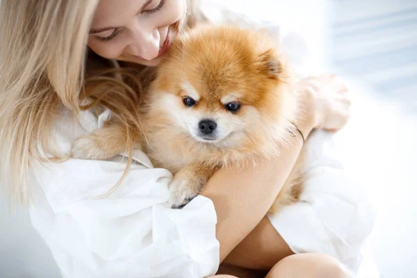 Güzel, genç, sarışın bir kadın köpeğiyle yerde oturuyor ve ona sarılıyor. Köpek soyu Pomeranian