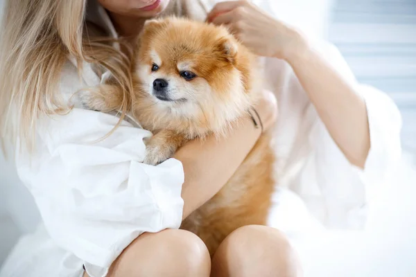 Güzel, genç, sarışın bir kadın köpeğiyle yerde oturuyor ve ona sarılıyor. Köpek soyu Pomeranian