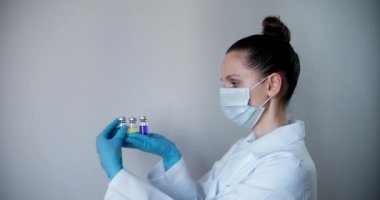 Genç beyaz kadın doktor ya da hemşire mavi koruyucu tıbbi maske takıyor, yakın plan portre. Ampul doktor ya da hemşire eli beyaz arka planda izole edilmiş. Sağlık hizmeti konsepti. Aşısı yeşil ve mor olan ampul..