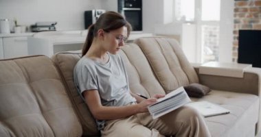 Mutlu esmer kadın evde çalışıyor, evde çalışıyor. Genç esmer bir kadın kanepede oturuyor, not defterine not alıyor. Karantina karantinası. Yakın plan kadın portresi