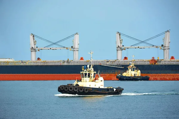 Буксир, помогающий грузовому судну — стоковое фото