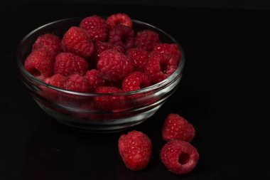 Siyah bir arka plan üzerinde bir cam kabın içinde ahududu