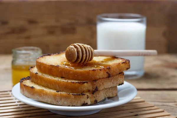 Жареный тост на белой тарелке с молоком и банкой меда на деревянном фоне — стоковое фото