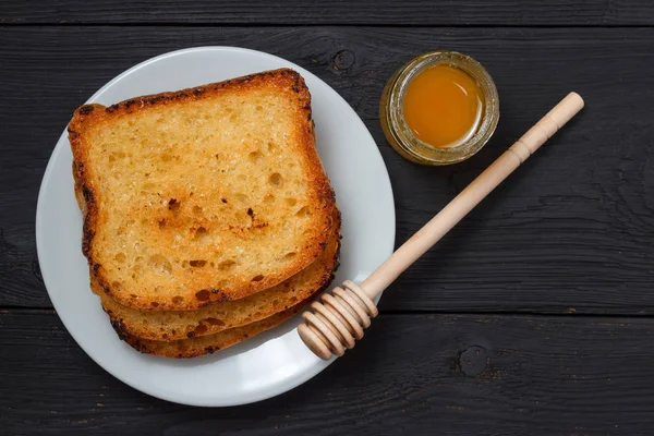 Tostadas con leche y un frasco de miel sobre un fondo de madera negro — Foto de Stock