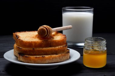 Tost bir kaşık bal, süt ve bal ile beyaz bir plaka üzerinde olabilir