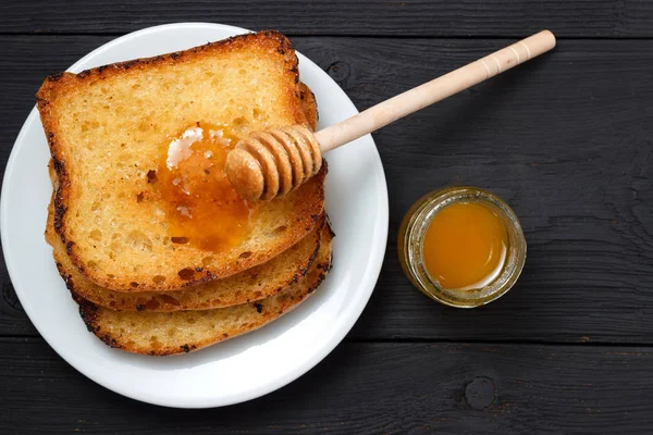 Drei Toastbrote auf einem weißen Teller mit Honig und einem Honiglöffel — Stockfoto