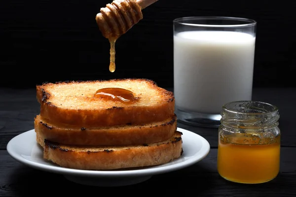Tostadas fritas con un vaso de leche, una lata de miel y una gota de miel en una cuchara — Foto de Stock