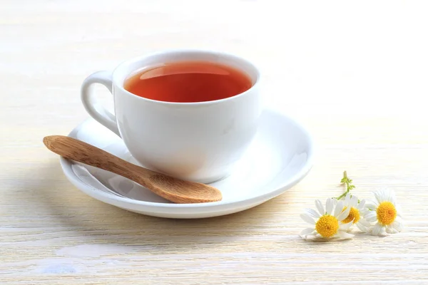 Tee mit Kamille und einem Holzlöffel auf einer Untertasse — Stockfoto