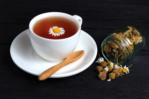 Xícara de chá com camomila em uma xícara branca em um fundo preto — Fotografia de Stock