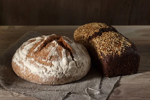 Yuvarlak ve siyah kare ekmek somun ve ahşap arka plan — Stok fotoğraf