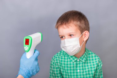 Hasta bir çocuk kızılötesi termometreyle ölçülür.