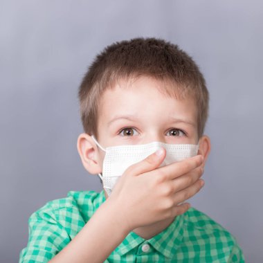Çocuk tıbbi maske takmış öksürüyor.