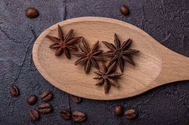 Anis, tahta bir kaşıkta, beton bir arka planda, kahve taneleriyle.