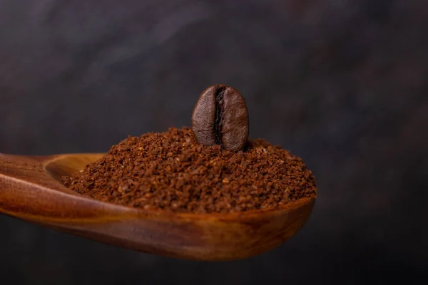 Grain coffee in a wooden spoon of ground coffe on a dark background