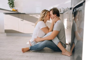 Güzel genç bir çift birlikte vakit geçiriyor. Mutfakta yerde oturarak kucaklaşın. Çok romantik.