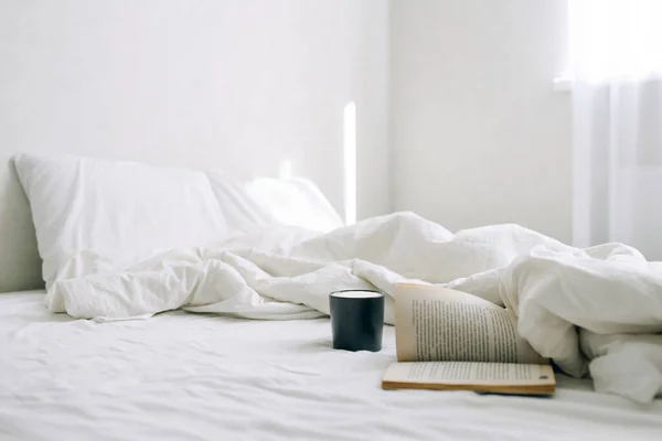 Hafif yatak odası, kahve ya da çay fincanı ve yatağın üzerinde açık bir kitap..