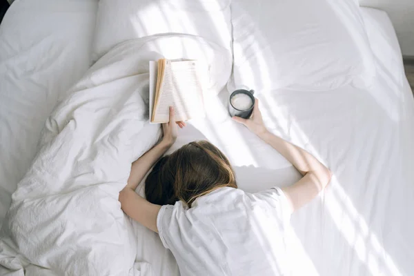 young girl student sleeping in bed with a book in her hands holding coffee in her hands. Can\'t get out of bed