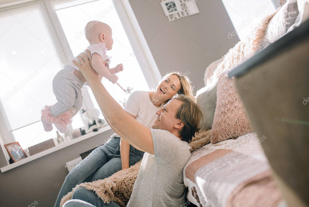 Happy family having fun together at home. Dad throws up his daughter, mom smiles at the background