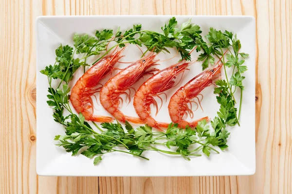 Çiğ karides ve beyaz plaka ve ahşap masa maydanoz