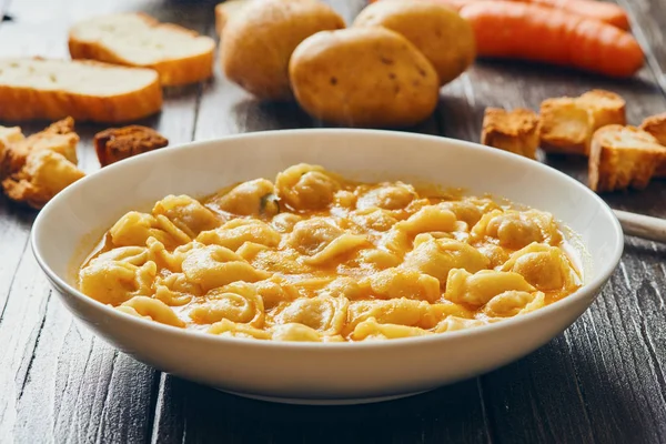 Sopa de tortellini em prato branco em mesa de madeira — Fotografia de Stock