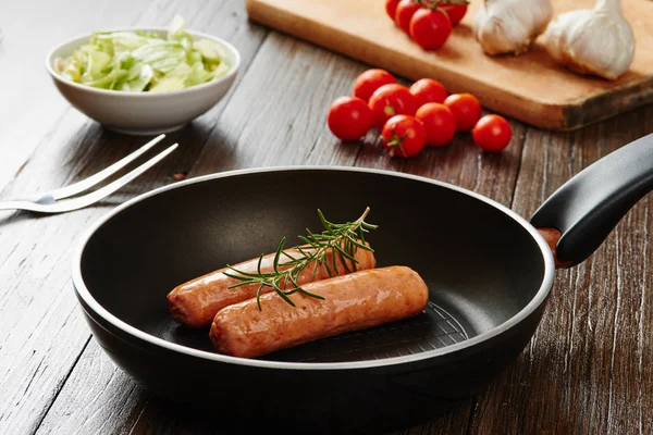 Salsicha crua em panela na mesa de madeira cercada por ingredientes — Fotografia de Stock