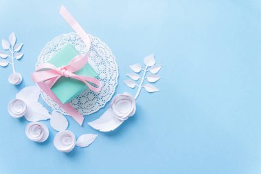 mavi zemin üzerine beyaz bir peçete ve beyaz kağıt çiçekler bir hediye